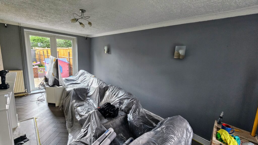 Living room painting in progress with furniture covered and dark wall finish applied