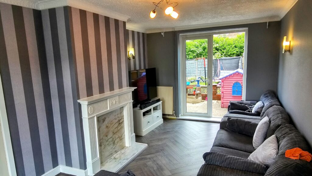 Finished living room with striped feature wallpaper, dark painted walls, fireplace and modern flooring