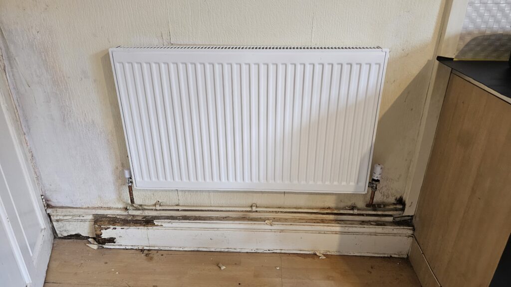 Damaged skirting board and exposed radiator pipework during preparation for repair and boxing