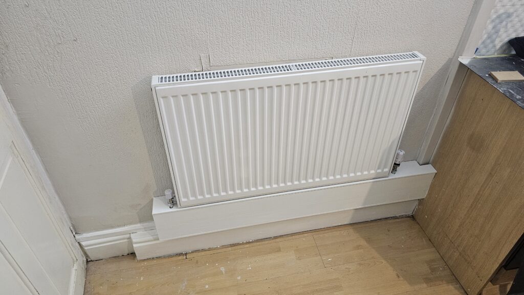 Custom radiator pipe boxing with repaired skirting board beneath a wall-mounted radiator