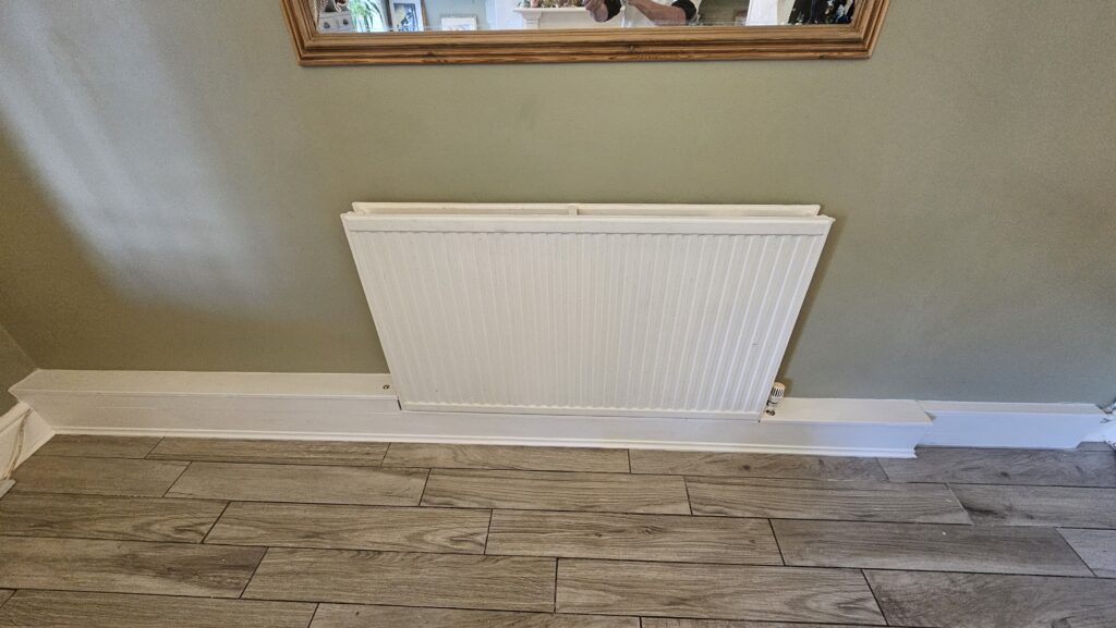 Finished custom radiator pipe boxing with clean skirting finish beneath a wall-mounted radiator