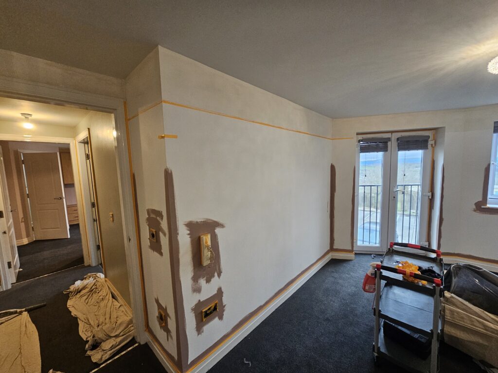 Living room painting project in progress with wall repairs and masking in place