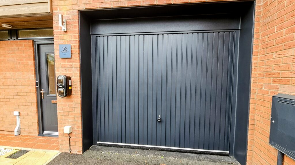 Metal garage door and UPVC front door spray-finished in a dark grey/black colour on a brick house.
