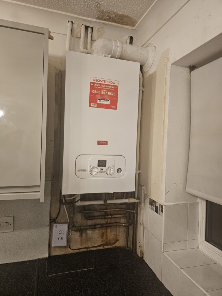 Boiler and exposed pipework in a kitchen corner before boxing in.