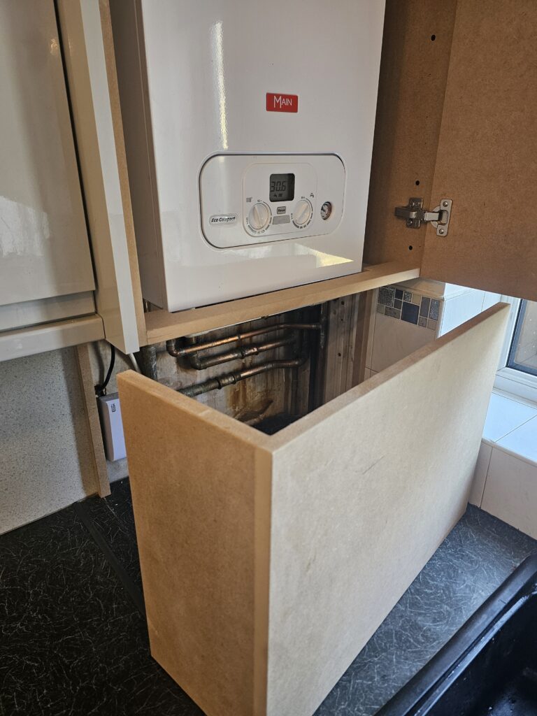 Boiler boxing with hinged access door and removable lower panel to reach pipework.