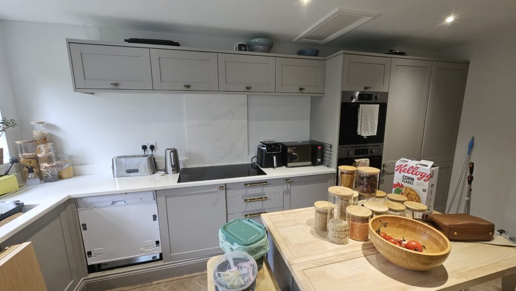Wide view of the existing grey kitchen and wooden island worktop before the custom shelves were installed.