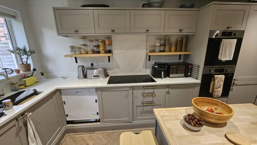 Wide view of the finished custom kitchen shelves with wood veneer finish, installed above the worktop and styled with glass storage jars.