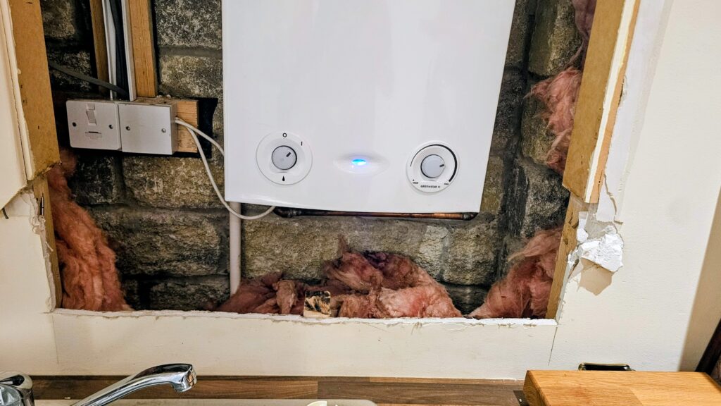 Close-up of rough plasterboard edges and exposed insulation beneath a newly installed boiler before custom cupboard doors were fitted.