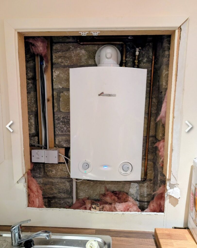 Existing boiler housing with exposed boiler, unfinished timber framing and rough plasterboard edges before custom cupboard doors were installed in Glossop.