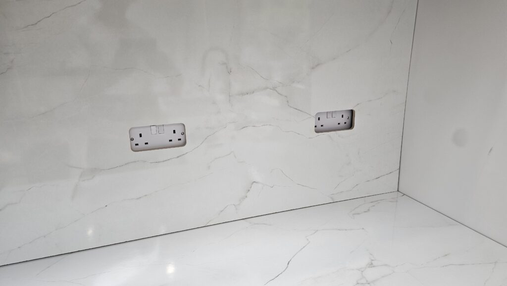 Finished double socket cut-outs accurately aligned in a marble-effect kitchen splashback panel