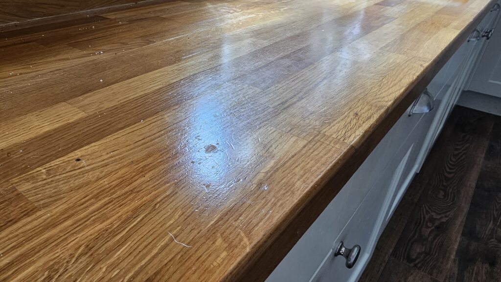 Worn solid oak kitchen worktop with scratches, dents and surface wear before restoration in Glossop.
