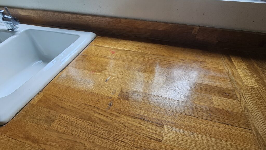 Solid oak kitchen worktop with paint splashes, black marks and worn finish before sanding and restoration.