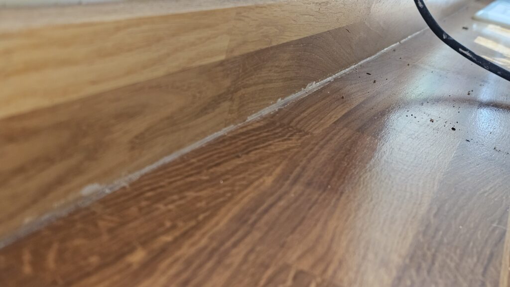 Old discoloured silicone sealant along the back edge of a solid oak kitchen worktop before restoration.