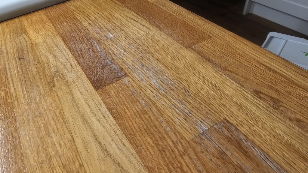 White water marks and worn finish on a solid oak kitchen worktop before sanding and refinishing.
