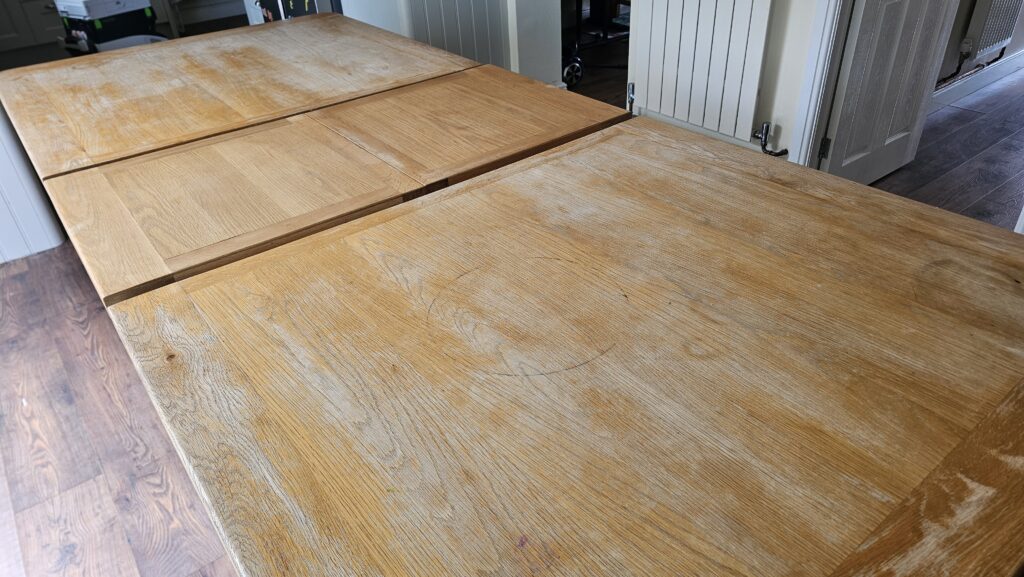 Solid oak dining table with sun bleaching, white patches and black marks before restoration.