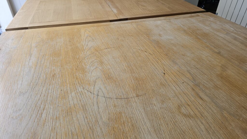 Close-up of a solid oak dining table showing sun bleaching, surface scratches and faded finish before restoration.