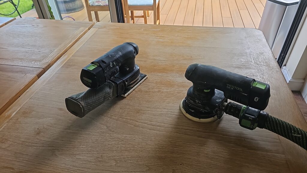 Festool orbital sanders removing the old finish from a solid oak dining table during restoration.
