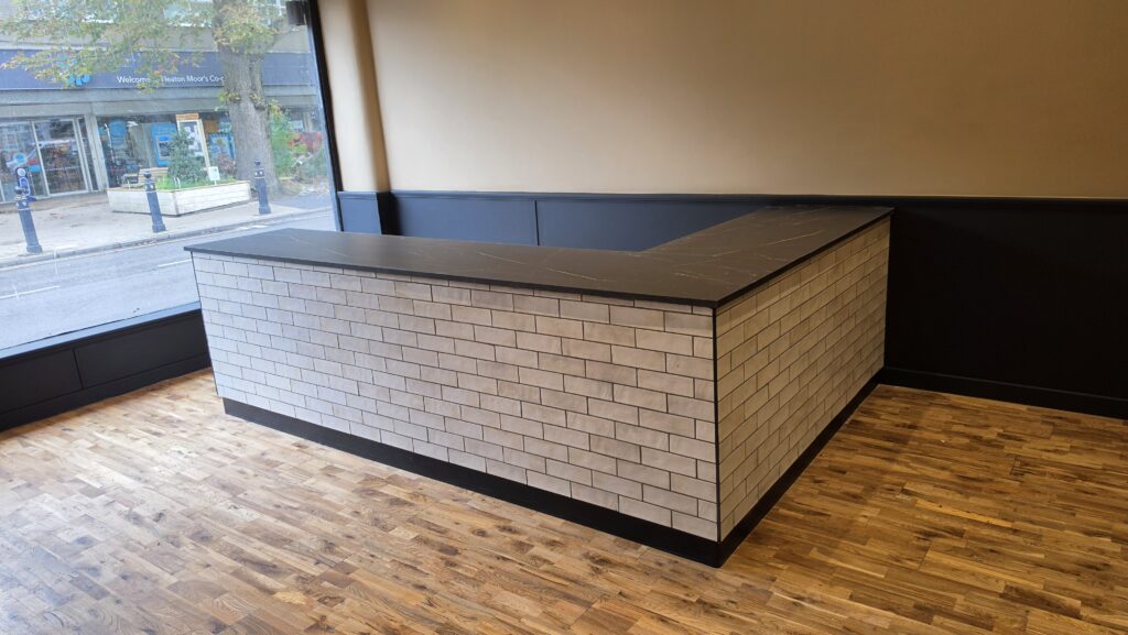 L-shaped bespoke café counter with white brick tiles and black worktop