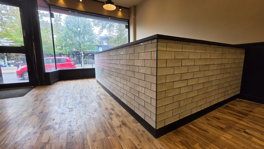 Close-up corner view of tiled café counter with black trim and plinth
